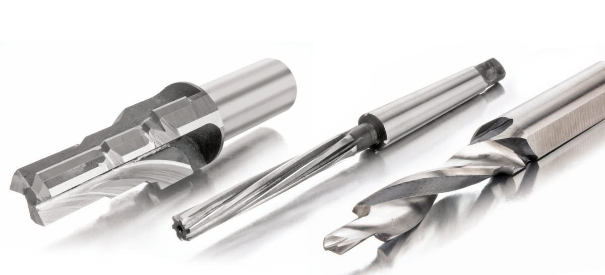 Three brazed carbide tools — a stepped counterbore, a taper-shank reamer and a drill — on a reflective surface.