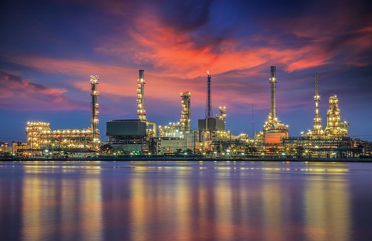 Refinery complex lit at dusk along a waterfront.